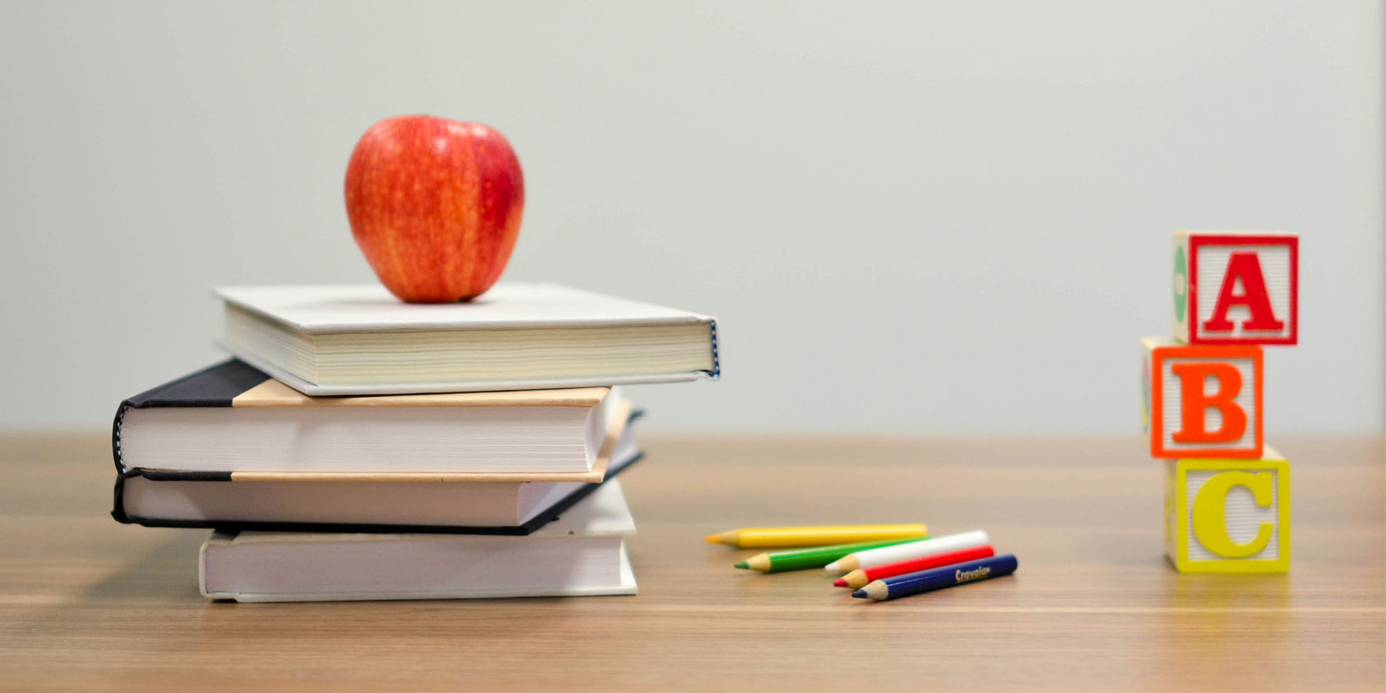 Photo of books, apple, colored pencils, and alphabet blocks on table.