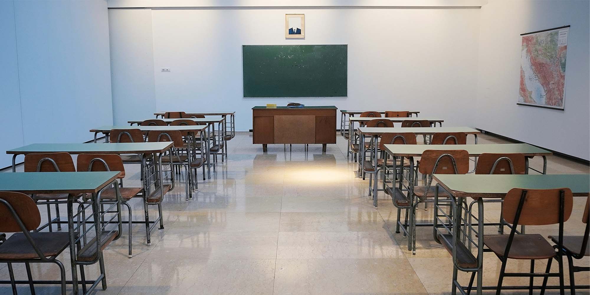 Empty classroom with a blank chalkboard in the background behind the teacher's desk.