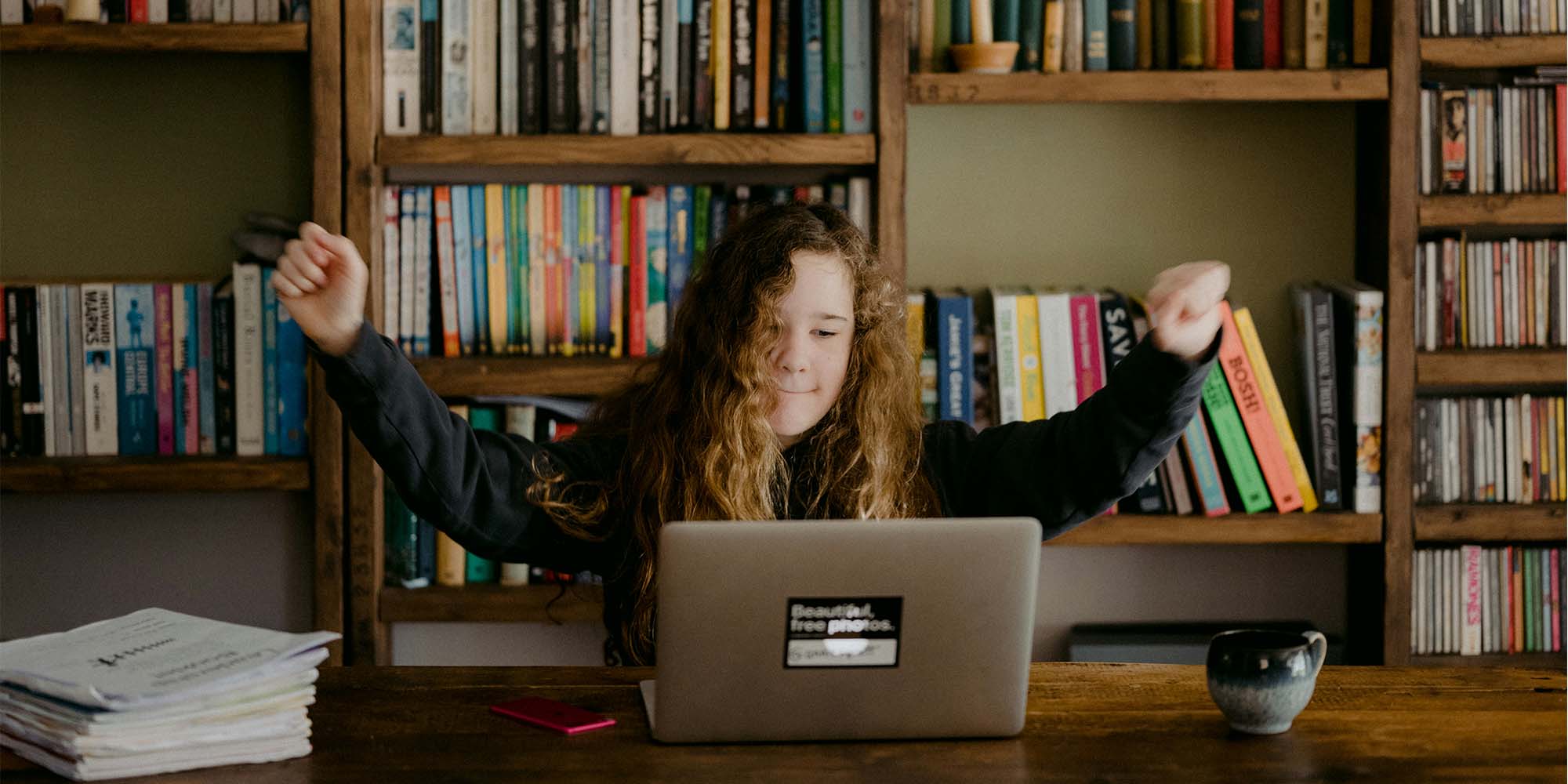 girl in front of laptop holding arms up in cheer